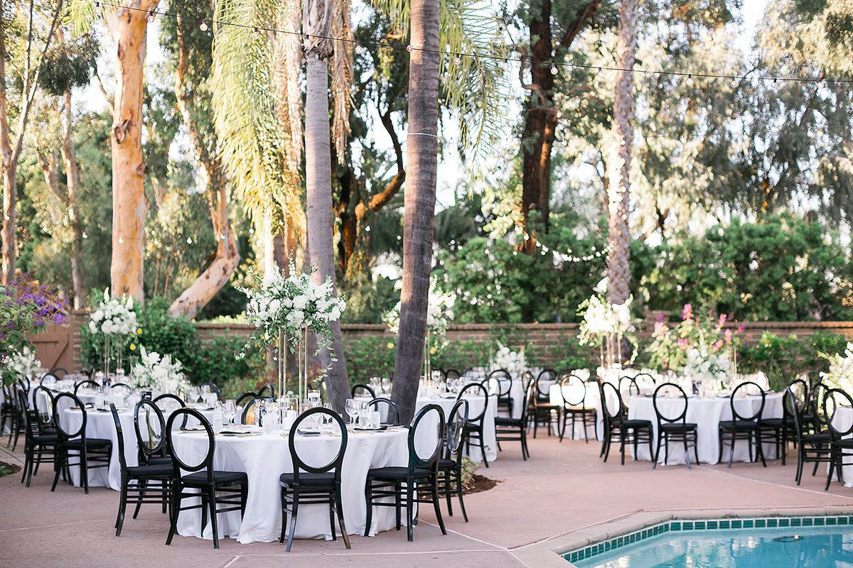 Outdoor reception tables with black chairs and tall white centerpieces beside the pool and palms at Rancho Valencia.