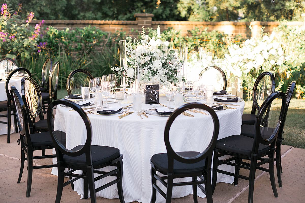 A round reception table set with black chairs, a low white floral centerpiece, and a black table number.