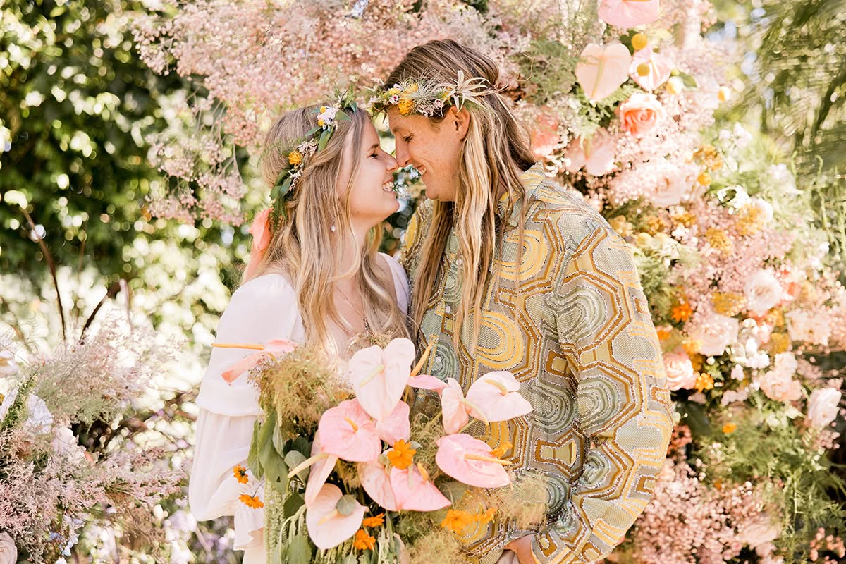 Emily and Evan share a kiss in front of lush pink garden florals.