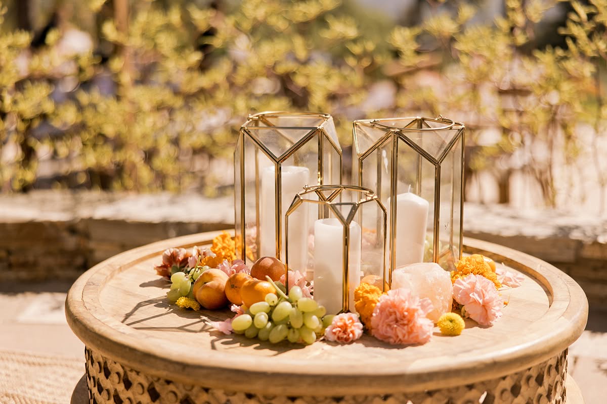 Round cocktail table with candle lanterns, fruit, and colorful floral accents for a garden wedding.