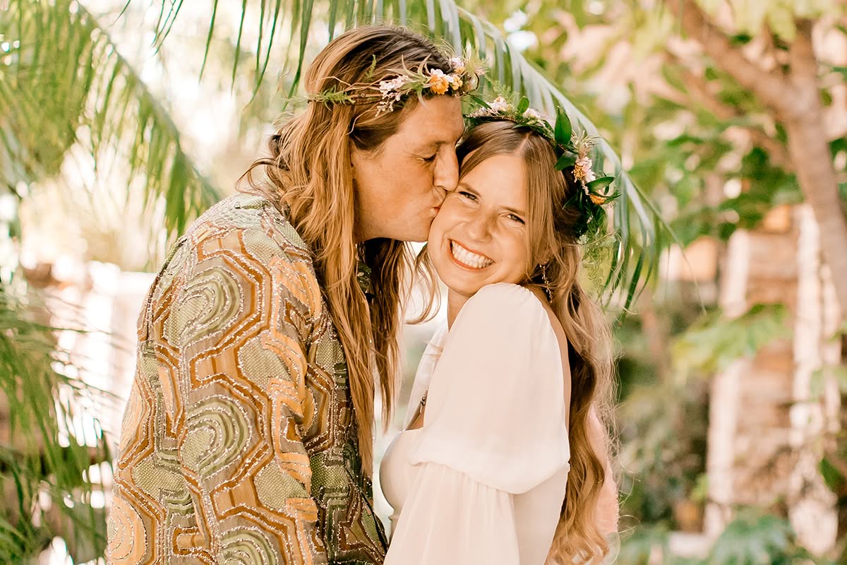 Emily and Evan smile together beneath tropical greenery during their garden wedding portraits.