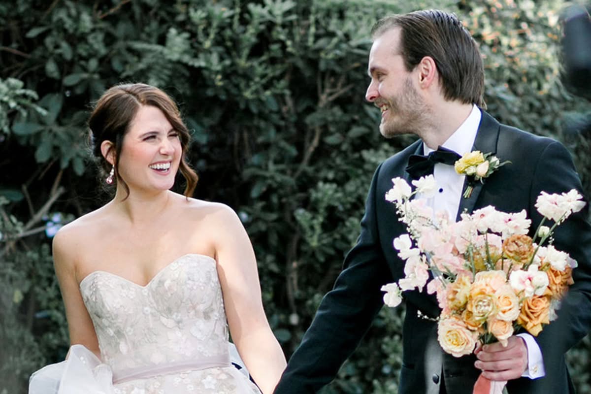 Bride and groom walking together outdoors with soft sunset-toned florals at Estancia La Jolla.
