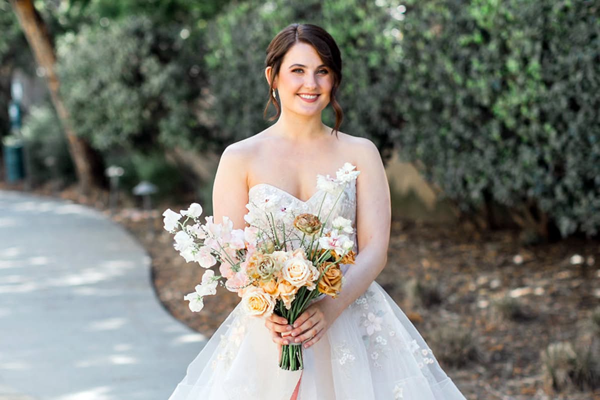 Bride holding a pastel bouquet while standing outdoors before her wedding ceremony.