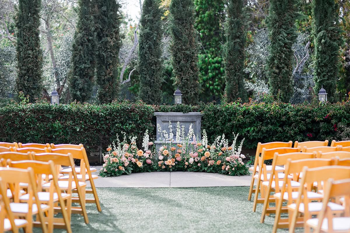 Outdoor ceremony setup with wooden chairs, greenery, and a floral ground arrangement.