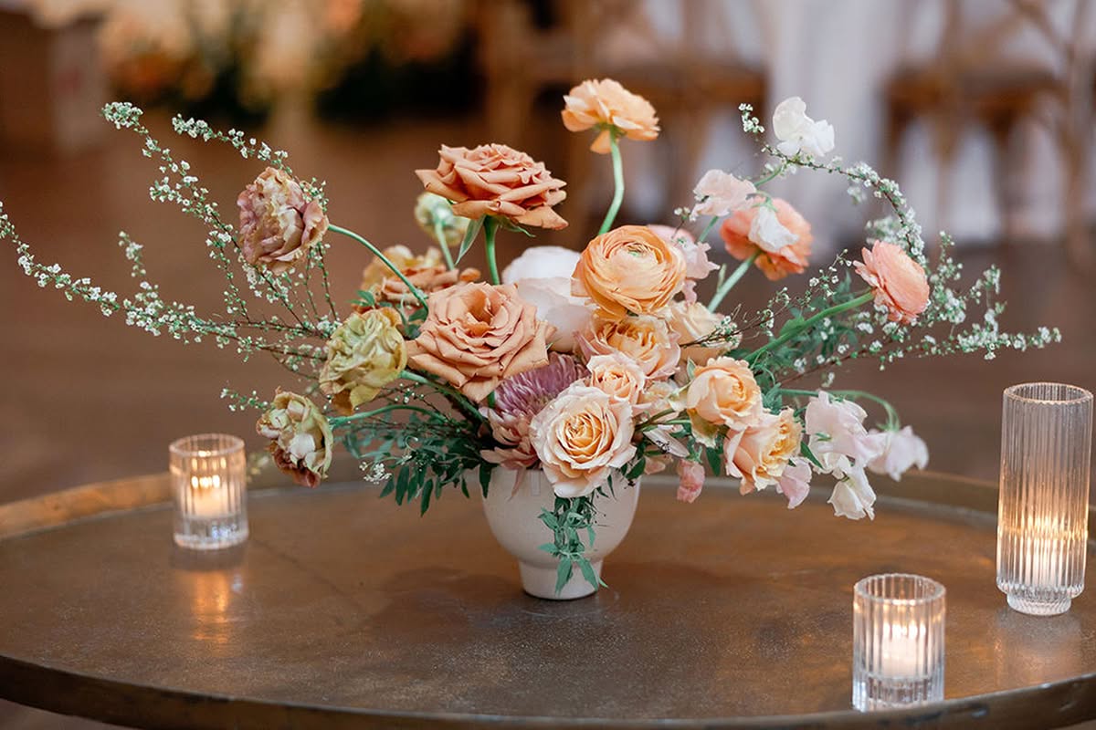 Close-up of peach and blush floral arrangement with candlelight.