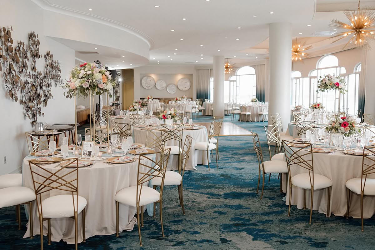 Elegant wedding reception ballroom at Loews Coronado Bay Resort with round tables, gold chairs, and coastal blue carpeting.