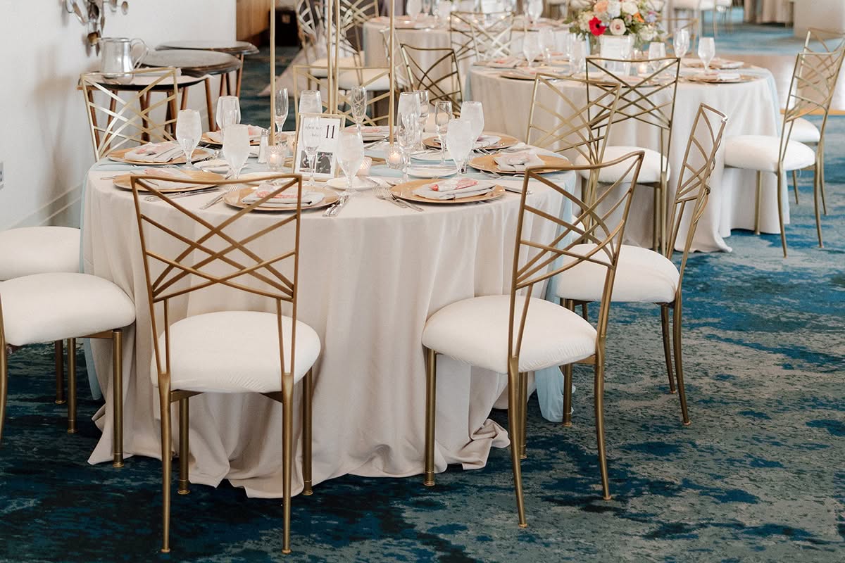 Wide view of a Loews Coronado Bay Resort wedding reception with round tables, gold chairs, and floral centerpieces.