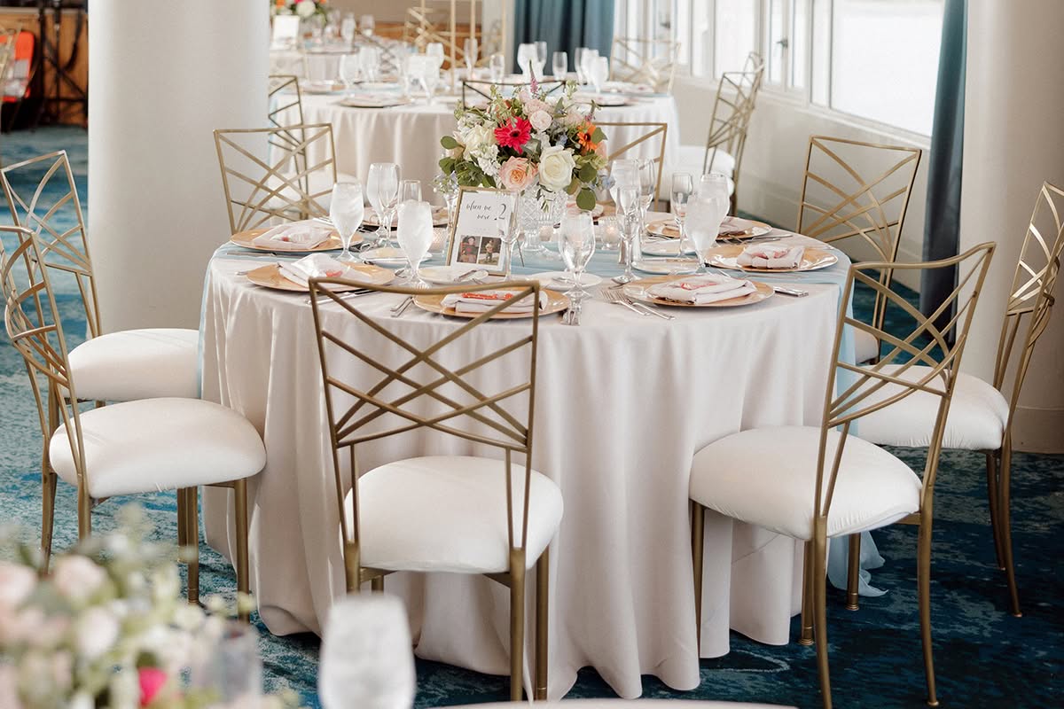 Round wedding reception table with floral centerpiece, gold chairs, and soft coastal light at Loews Coronado Bay Resort.
