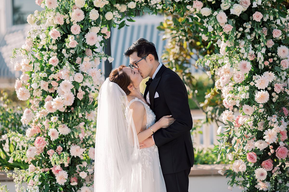 Bride and groom kissing beneath a lush pink and white floral arch at Hotel del Coronado.