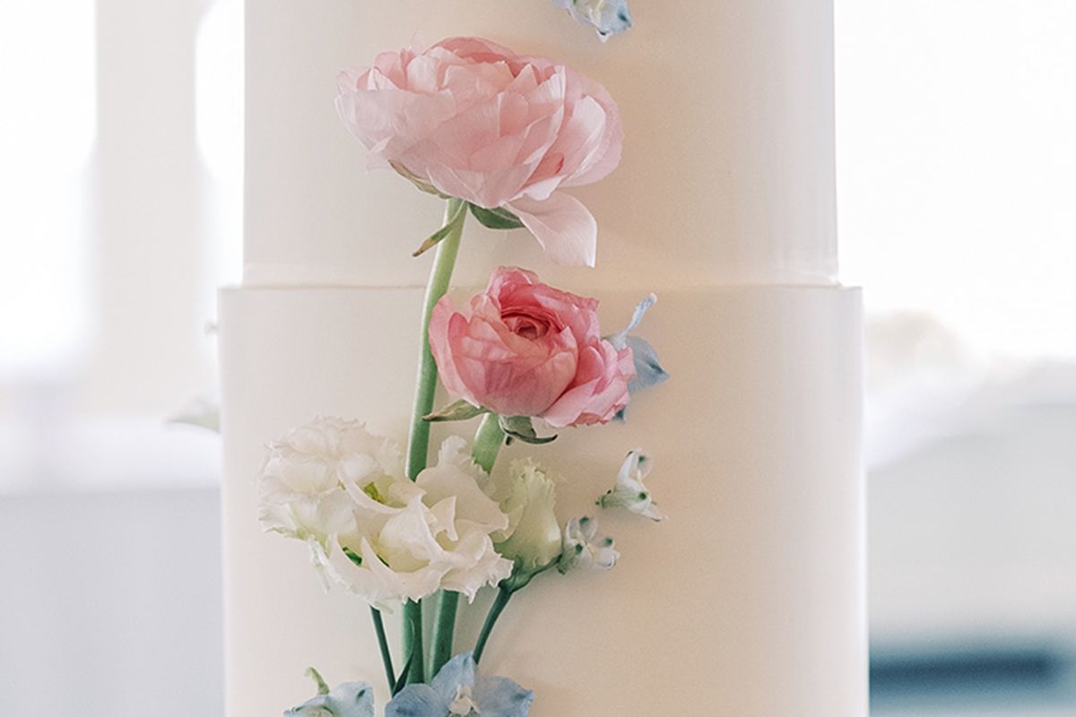 A tiered white wedding cake decorated with pink and blue pastel florals.