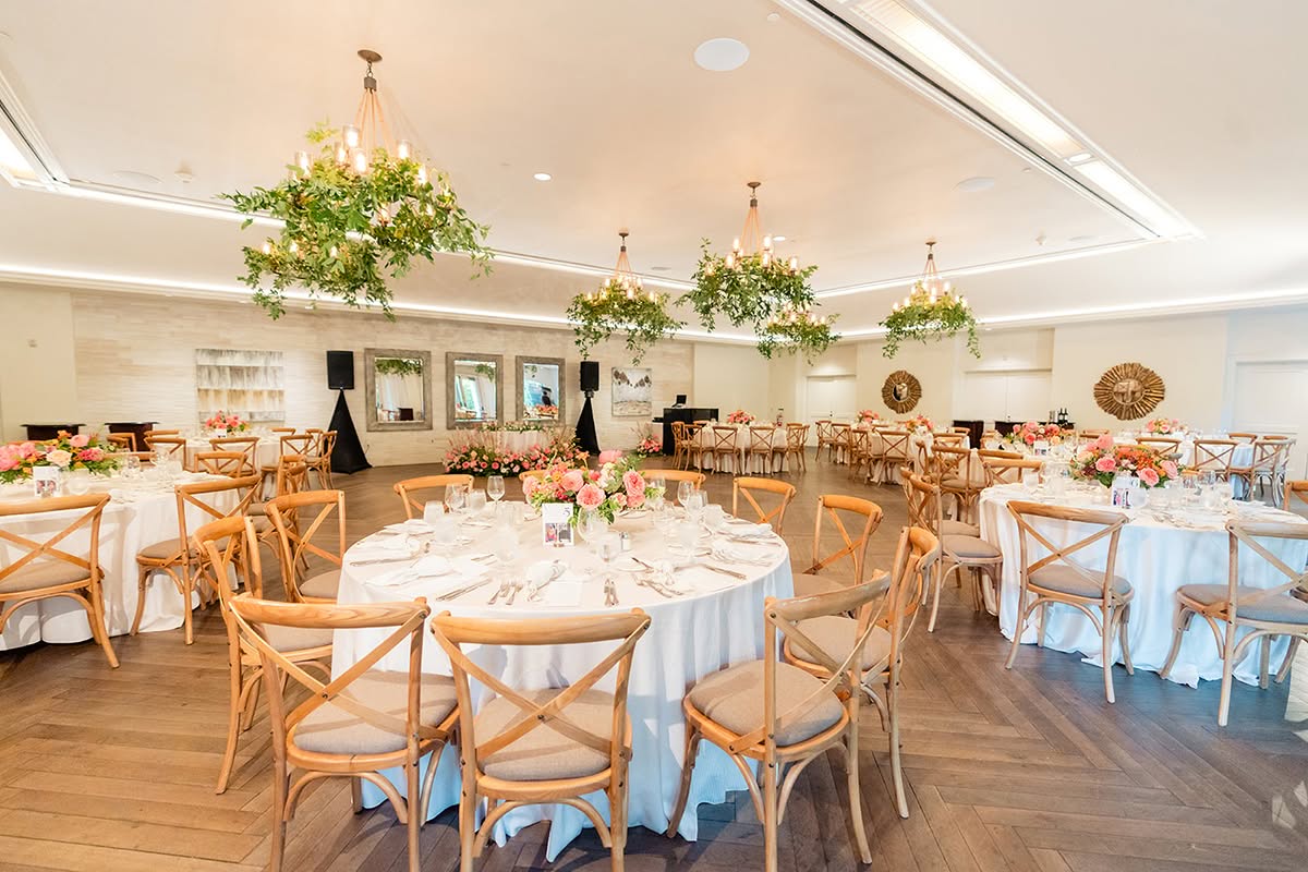 Elegant wedding reception at Estancia La Jolla Hotel & Spa with round tables, wood chairs, and hanging greenery.