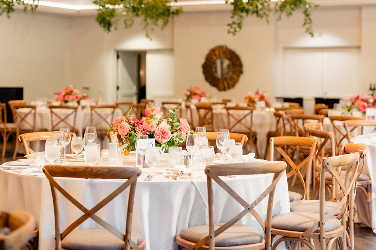 Round wedding reception tables with wood chairs, white linens, and hanging greenery at Estancia La Jolla Hotel & Spa.