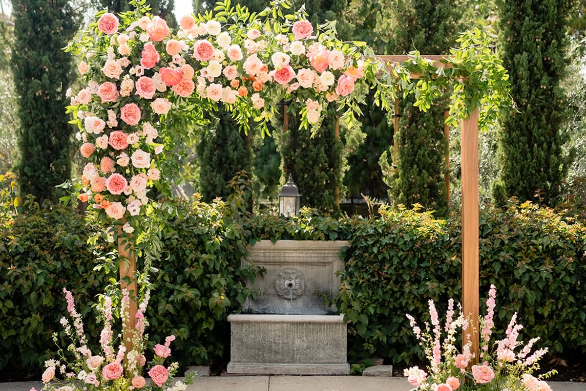 Floral wedding ceremony arch set in a garden courtyard at Estancia La Jolla Hotel & Spa.