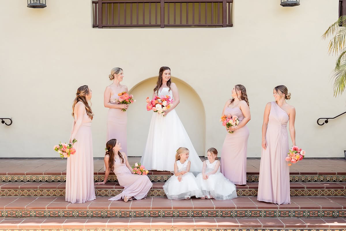 Bride standing with bridesmaids in soft pink dresses and flower girls on the steps at Estancia La Jolla.