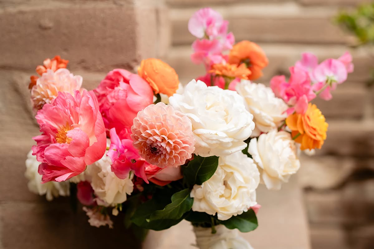 Bright wedding bouquet with pink, orange, and yellow flowers resting on stone steps.
