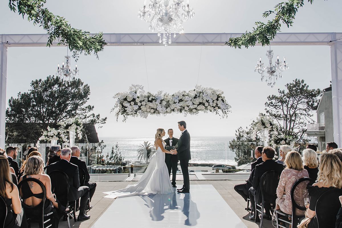 Bride and groom standing during their rooftop wedding ceremony overlooking the ocean.