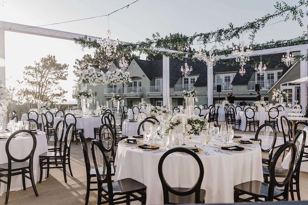 Rooftop reception setup with black chairs, white florals, and seaside architecture.