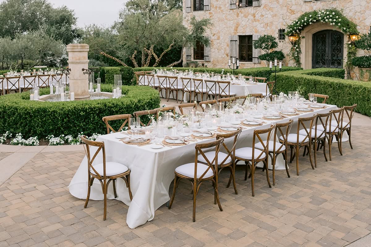 Courtyard reception setup with long tables, a stone fountain, and European-style architecture.